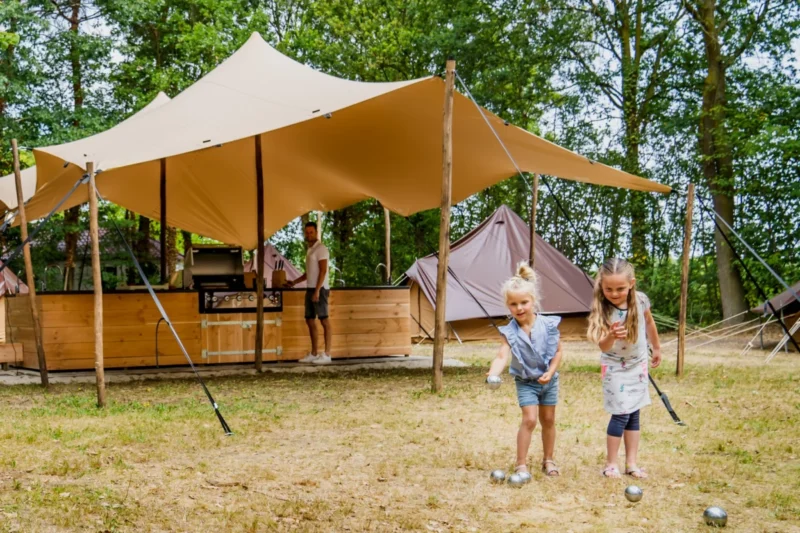 Glampingtent met overdekt terras en spelende kinderen op Vakantiepark BreeBronne